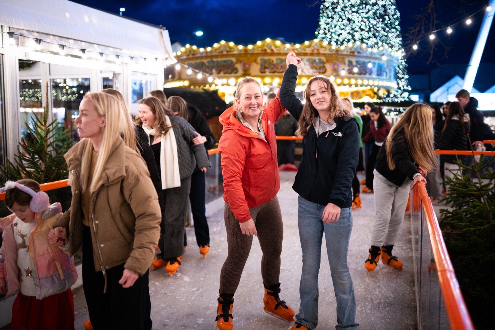 Skaters celebrating on the ice in front of the carousel and lit Christmas tree